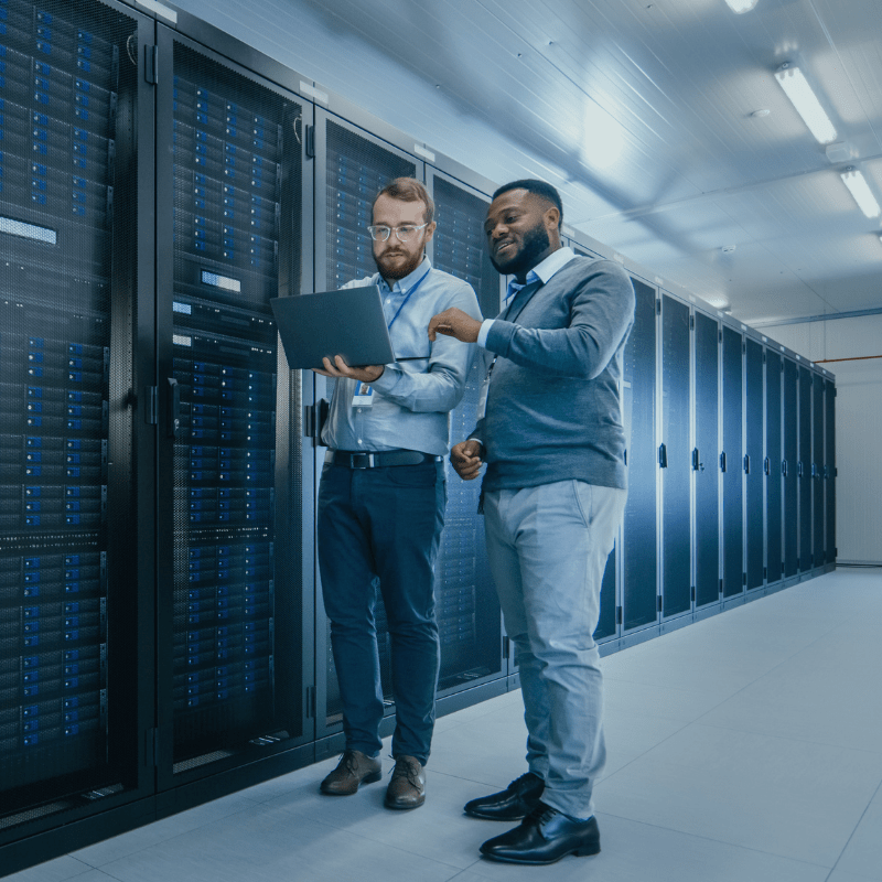 Two employees standing in a data center filled with servers.