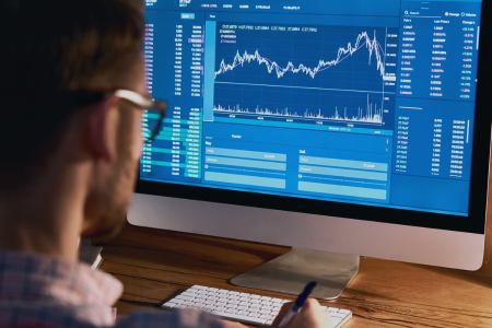 A male employee reviews market data on a desktop computer.