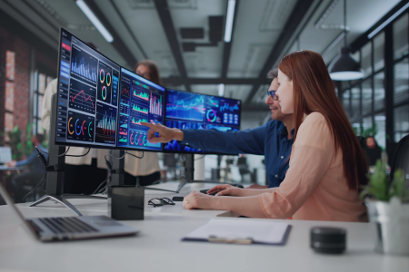 A female employee reviews market data on desktop computer in office. 