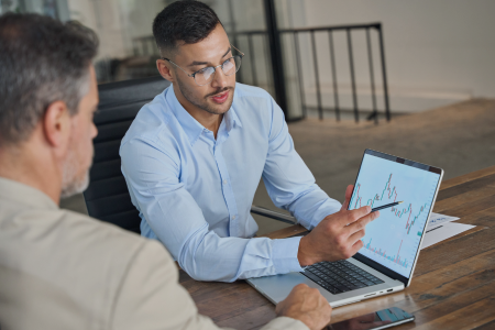 Two male colleagues review market data on a laptop. 