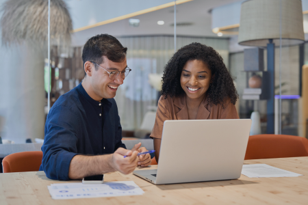 One male and one female employee look at a laptop together. 