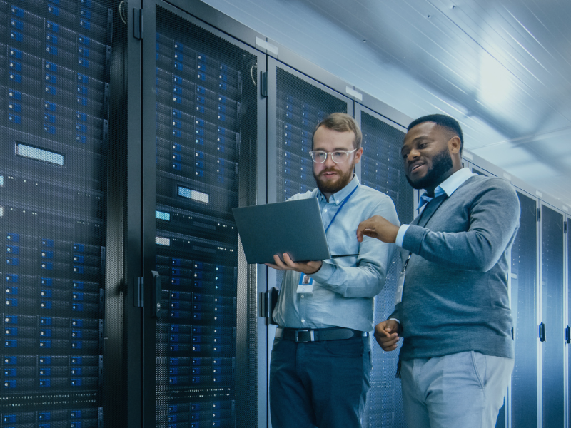 Two employees standing in a data center filled with servers. 